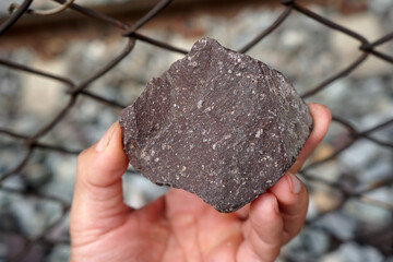 Raw specimen of rhyolite extrusive igneous rock stone on Geologist's hand. The paving stones are...