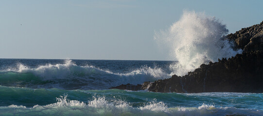 huge beautiful wave is breaking at the coastline while a breeze blows the spit water out of the sea...
