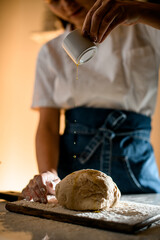 female hand pours oil from on dough on a wooden cutting board