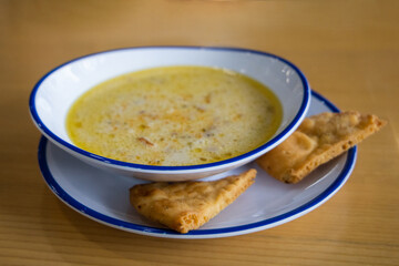 Greek food lemon chicken soup in a bowl the winter on a restaurant dining table with fried pita crisp crackers as a garnish