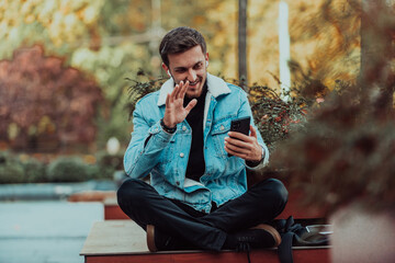 A gappy student sitting in a park using a smartphone and wireless headphones
