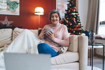 Happy senior woman with cup of coffee watching movie in laptop