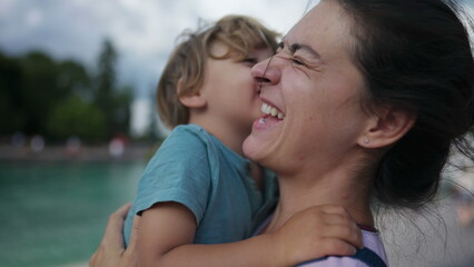 Fototapeta premium Funny mother and son moment. Little boy kissing mom in cheek pretending to be disgusted. Family lifestyle bonding moment. Authentic real life