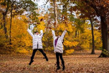 Fototapeta premium Two young asian girls tossing leaves in the air 