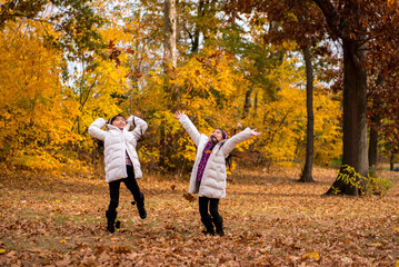 Fototapeta premium Two young asian girls tossing leaves in the air