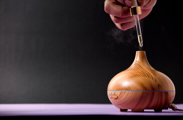 wooden air freshener with steam of natural essences, man's hand with dispenser, purple and black background