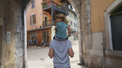 Fototapeta na wymiar Back of child on father shoulders visiting traditional European city street. Family on vacations traveling to new place