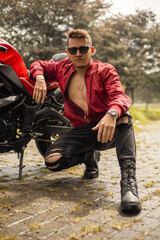 Fototapeta premium attractive latin male model next to his motorcycle, adventurous lifestyle, casual and youth fashion, transportation and hobbies in the day, roads