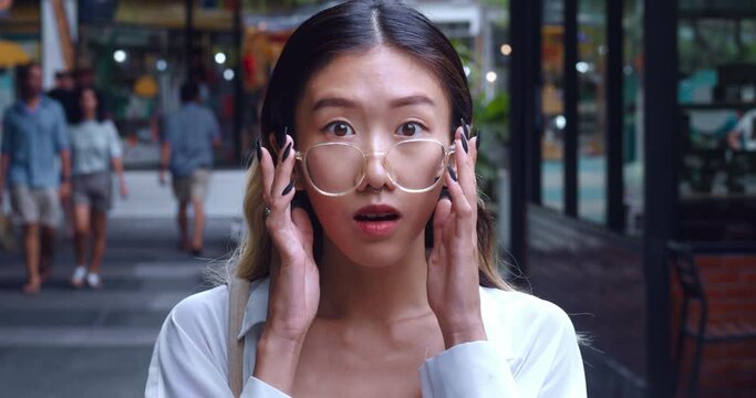 Shocked young woman takes off glasses and looks surprised at the camera. Portrait Asian woman in glasses 20 years old shocked by what she saw and smiling. Concert person suddenly surprised and shocked