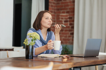 confident female entrepreneur works in office or coworking, drinks coffee and talks on phone. successful business career. young woman is working on laptop online or dating. modern lady