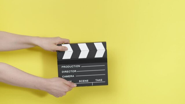 Film clapperboard in the hands of a yellow background.