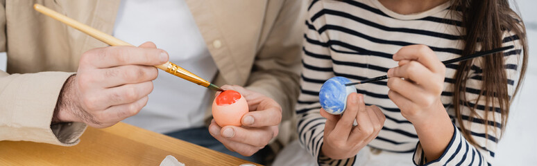 Cropped view of man and kid panting Easter eggs at home, banner.
