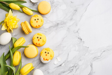 Set of easter macaroon chicks with yellow tulips, daffodils and eggs over marble background. Top view, copy space. Easter treat