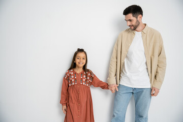Smiling man holding hand of daughter on white background.