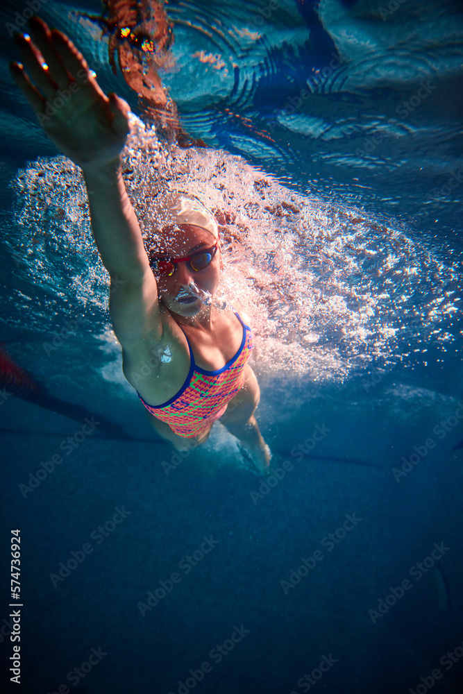 Wall mural dynamics. young sportive woman, professional swimmer training in swimming pool indoor. wearing cap a