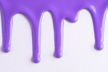Violet liquid drops of paint color flow down on white canvas. Abstract art. Lilac paint dripping on the white wall with copy space.