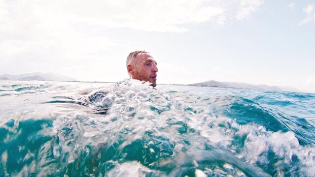 Man swims in the open sea. Splitted above and underwater view of the athlete swimming in the water