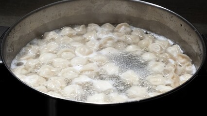 Small size meat dumplings are boiling in a pot on the stove. Pelmeni are the traditional national Russian cuisine. Italian ravioli. Food for children. Dish for kid. Cooking lunch or dinner for family