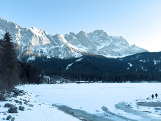 the beautiful eibsee in the foreground at the valley station of the zugspitzbahn in the south of germany where the mountains are illuminated by the sun and are covered with snow