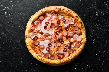 Pizza with sausages, bacon and cheese. classic pizza On a black stone background. Top view.