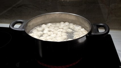 Small size meat dumplings are boiling in a pot on the stove. Pelmeni are the traditional national Russian cuisine. Italian ravioli. Food for children. Dish for kid. Cooking lunch or dinner for family