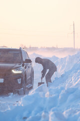 A man with a shovel digs out a car stuck in the snow. 