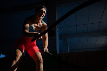 Athletic woman doing double wave exercise with ropes in crossfit gym.
