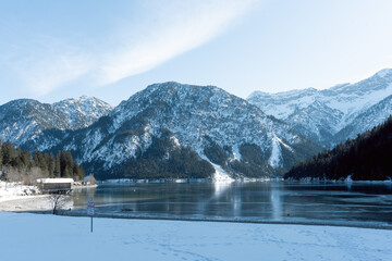 the beautiful lake plansee photographed in the day with the mountains covered with snow and the lake plansee in the foreground with crystal clear water