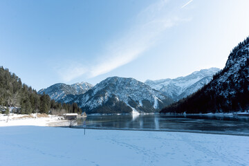 the beautiful lake plansee photographed in the day with the mountains covered with snow and the lake plansee in the foreground with crystal clear water