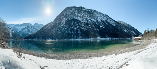 the beautiful lake plansee photographed in the day with the mountains covered with snow and the lake plansee in the foreground with crystal clear water