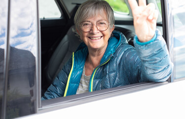 Portrait of attractive happy senior woman sitting in the car as passenger looking at camera smiling.
