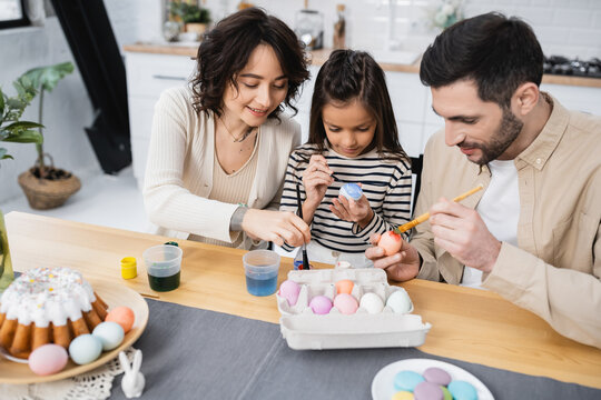 Smiling woman coloring Easter egg near family and food at home.