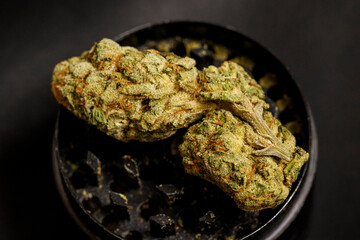 Close up of high quality marijuana bud with trichomes and crushed weed for chopping cannabis on a black table detail