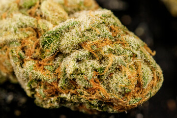 Macro detail of high quality marijuana bud with trichomes and crushed weed for chopping cannabis on a black table detail