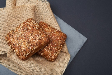 Two freshly baked rustic square shaped bread buns with sesame seeds on the vintage rustic country style sackcloth grey stone plate and solid fond plain black background