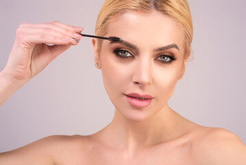 Eyebrow shaping, woman combs eyebrows with a brus. Eyebrow line. Makeup and cosmetology concept. Female model with long eyelashes and thick eyebrows. Perfect shaped brow. - obrazy, fototapety, plakaty