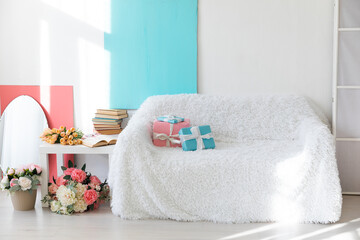 Fototapeta na wymiar white sofa with gifts coffee table with flowers and books in a bright room interior blue as backgrounds