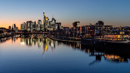 Fototapeta na wymiar Illuminated city skyline in the evening under the clear sky with the river in the foreground