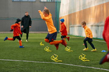 Boys, children, football players doing exercises, warming up before training session with coach on...