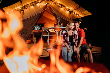 Obraz na płótnie Canvas Happy lovely couple relaxing in glamping on evening near cozy bonfire. Luxury camping tent for outdoor recreation and recreation. Lifestyle concept