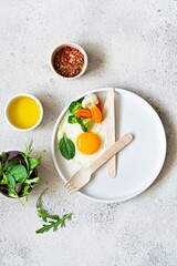 Healthy breakfast of fried egg and boiled vegetables with spinach on a light background.