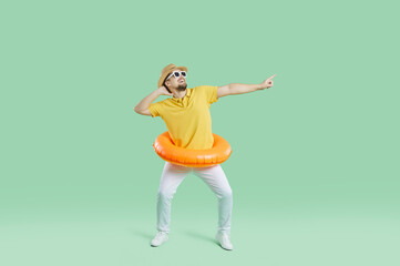 Fototapeta na wymiar Funny cheerful man with inflatable circle for swimming having fun on light green background. Full length of joyfully excited millennial guy having fun dancing while enjoying summer vacation. Banner.