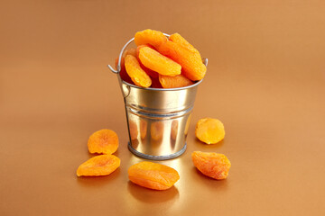A small metal bucket filled with dried apricots on a golden background. Dried apricots as an ingredient.