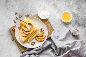 Delicious fresh baked pancakes with honey and fruits on a concrete background