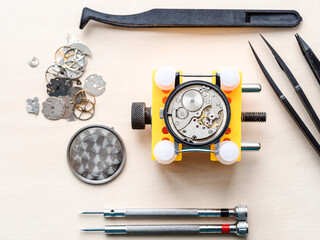 top view of open watch in yellow holder and tools on wooden table in watchmaker workshop