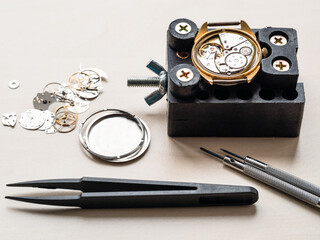 tools and open watch in holder on wooden table in watchmaker workshop