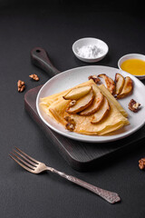 Delicious fresh baked pancakes with honey and fruits on a concrete background
