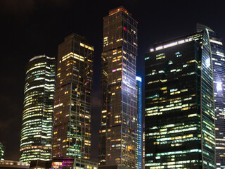 view of illuminated glass skyscrapers in Moscow city business district in evening from Taras Shevchenko embankment of Moskva river - obrazy, fototapety, plakaty