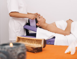 Side view of a relaxed young girl receiving a facial massage with bamboo canes by a professional masseuse. Concept of health and wellness.