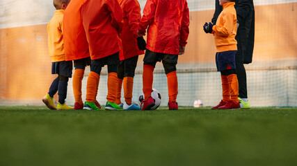 Cropped image of male legs on grass of sports field outdoors. Children playing football with coach. Concept of sport, childhood, active lifestyle, hobby, sport club